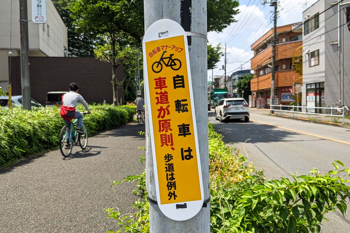 自転車は歩道を走りましょう、という看板を無視して歩道を走る自転車